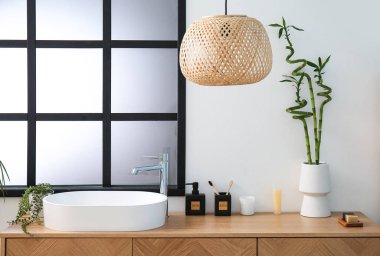 Masada beyaz lavabo, banyo aksesuarları ve bambu saplı vazo var.