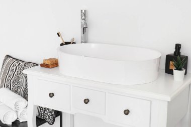 Banyodaki aksesuarlı lavabo, odanın ışık duvarının yanındaki masada.