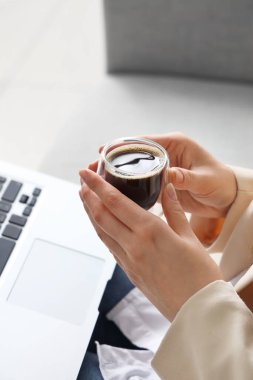 Kanepede oturan modern dizüstü bilgisayarı ve bir bardak lezzetli kahvesi olan bir kadın.