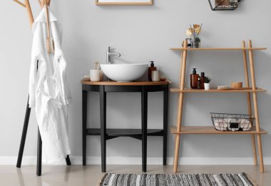 Banyonun içinde raf ünitesi, lavabo kasesi ve banyo aksesuarları var.