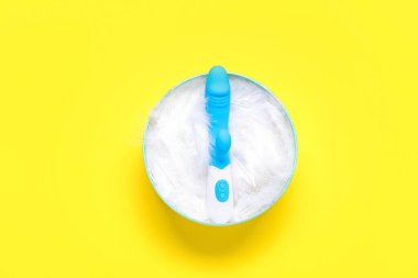 Sarı arka planda tüyleri ve vibratörü olan hediye kutusu.