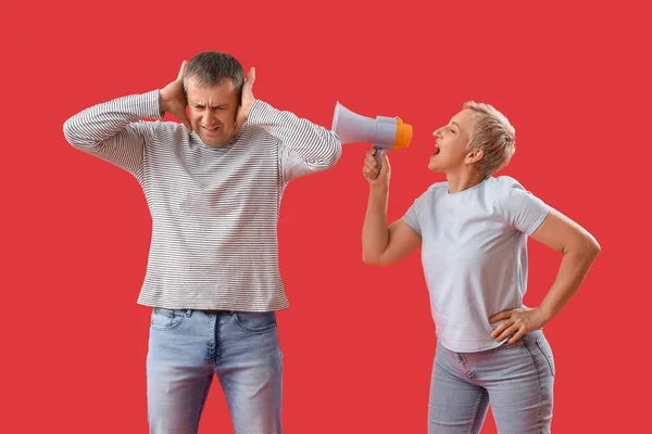 Mature woman with megaphone shouting at her husband on red background
