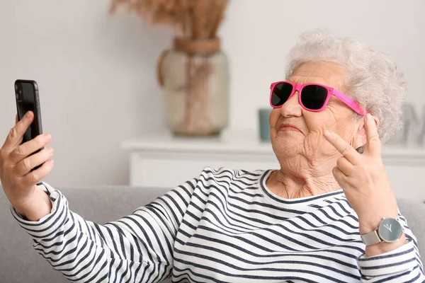 Güneş Gözlüklü Cep Telefonlu Yaşlı Kadın Evde Selfie Çekiyor — Stok fotoğraf