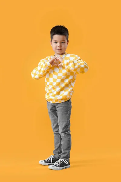 黄色の背景に彼の手でハートを作るセーターでかわいい男の子 — ストック写真