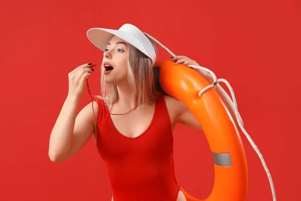 Female lifeguard with whistle and ring buoy on red background