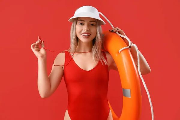 Female lifeguard with whistle and ring buoy on red background