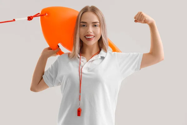 Female lifeguard with rescue buoy showing muscles on light background