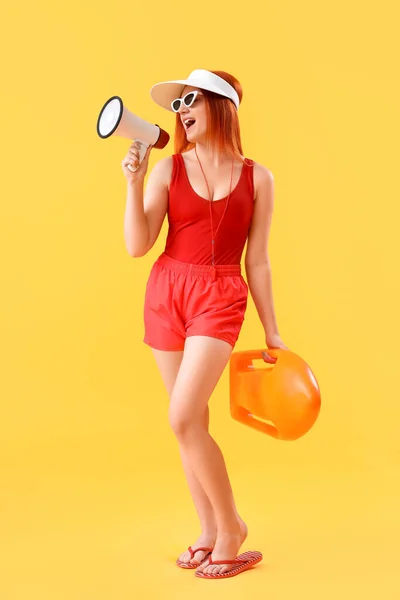 Female lifeguard with rescue buoy shouting into megaphone on yellow background