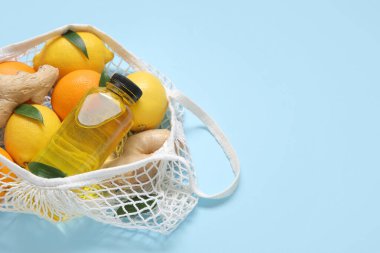 Mavi arka planda taze limon, portakal, zencefil ve bir şişe meyve suyu olan ağ torbası, yakın plan.