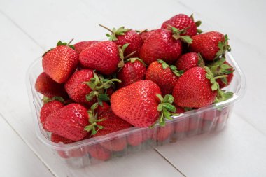 Hafif ahşap arka planda taze çilekli plastik kap, yakın plan.