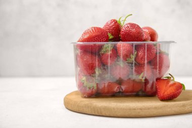 Hafif arka planda taze çilekli plastik konteynır, yakın plan.