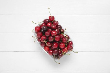 Hafif ahşap arka planda taze kirazlı plastik kap.