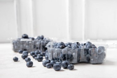 Beyaz zemin üzerinde taze yaban mersini olan plastik kaplar, yakın plan.