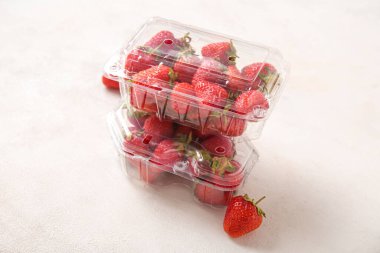 Açık arkaplanda taze çilek bulunan plastik kaplar.