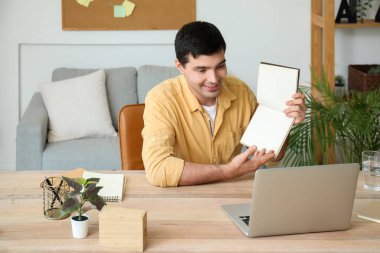 Not defteri olan genç bir adam evde iş görüşmesi yapıyor.