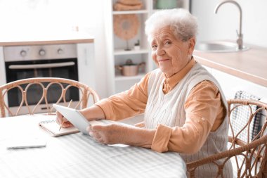 Mutfaktaki masada tablet bilgisayarı olan son sınıf öğrencisi kadın.