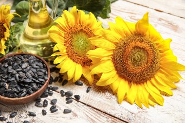 Güzel ayçiçekleri, tohumlu kase ve beyaz ahşap arka planda bir sürahi yağ.