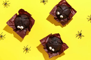 Cadılar Bayramı kutlaması için sarı arka planda lezzetli çikolatalı kekler ve örümcekler.