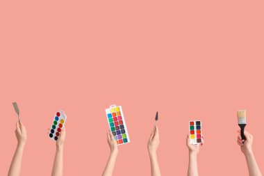 Pembe arka planda sanatçı malzemeleri olan kadın eller.