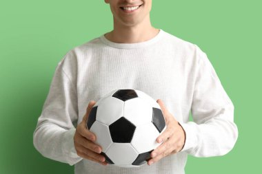 Yeşil arka planda futbol topu olan genç adam, yakın plan.