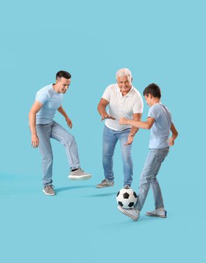 Küçük çocuk, babası ve dedesiyle mavi arka planda futbol oynuyor.