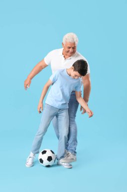 Küçük çocuk ve dedesi mavi arka planda futbol oynuyorlar.
