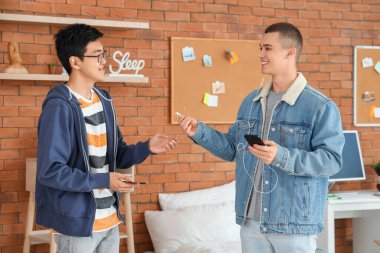 Genç çocuk yurt odasında oda arkadaşına kulaklık veriyor.