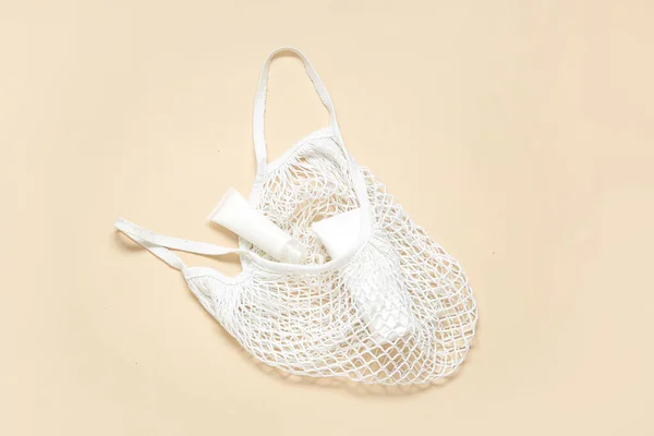 Mesh bag with tubes of cosmetic products on beige background