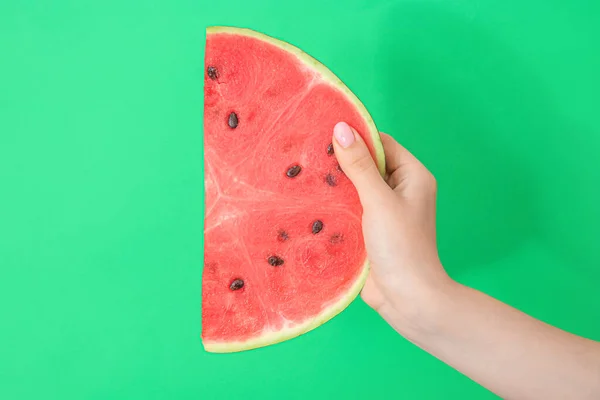 Female hand with piece of ripe watermelon on green background