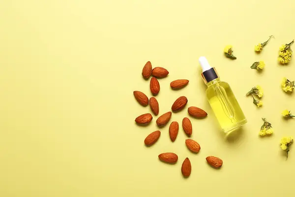 Bottle of cosmetic oil with almond and beautiful flowers on yellow background