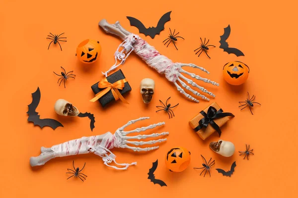 Composition with skeleton hands, gift boxes, skulls, paper bats and spiders for Halloween celebration on orange background