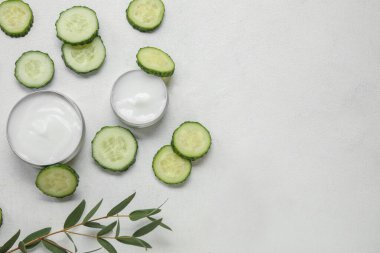 Doğal krema kavanozları, salatalık dilimleri ve açık arkaplanda okaliptüs dalıyla kompozisyon