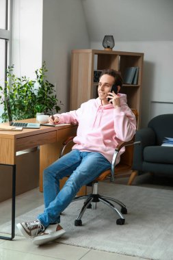 Ofiste cep telefonuyla konuşan serbest çalışan erkek.