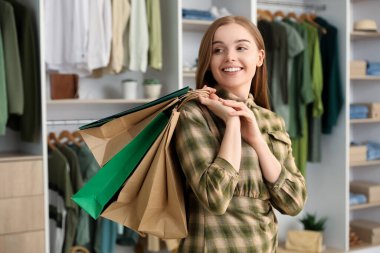 Alışveriş poşetleriyle butikte mutlu genç bir kadın.