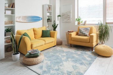 Sörf tahtası, sarı kanepesi ve koltuğu olan bir oturma odası.