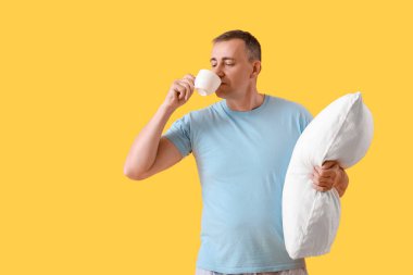 Yumuşak yastıklı olgun bir adam sarı arka planda kahve içiyor.