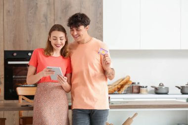 Tablet bilgisayarı ve hediye kartı alışverişi yapan genç bir çift mutfakta.