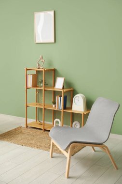 Kitaplı, dekorlu, sandalyeli ve boş çerçeveli raf odası yeşil duvarda asılı.