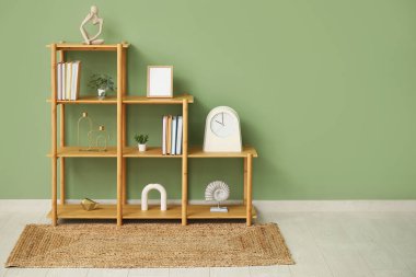 Kitapları, saati ve boş çerçevesi olan raf ünitesi yeşil duvarın yanında.