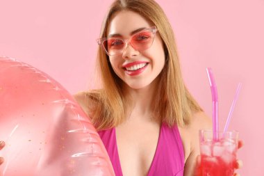 Şişirilebilir yüzüğü ve pembe arka planda lezzetli çilekli mojito 'su olan güzel genç bir kadın.
