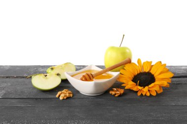 Bir kase tatlı bal, elma, ayçiçeği ve ceviz, beyaz arka planda, siyah ahşap masada.