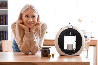 Mutfakta kahve makinesi olan olgun bir kadın.