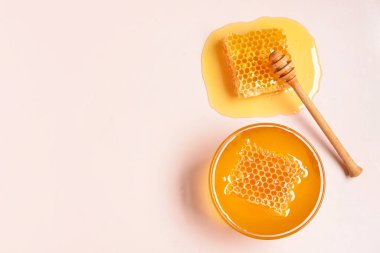 Tatlı ballı cam kase ve pembe arka planda taraklar