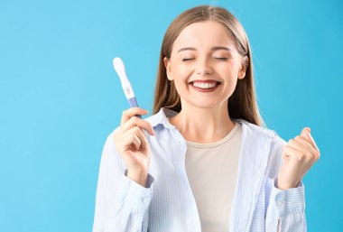 Mavi arka planda pozitif hamilelik testi olan mutlu genç bir kadın.