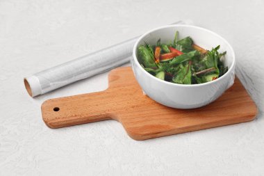 Hafif arka planda plastik gıda ambalajıyla kaplı bir kase taze salata.