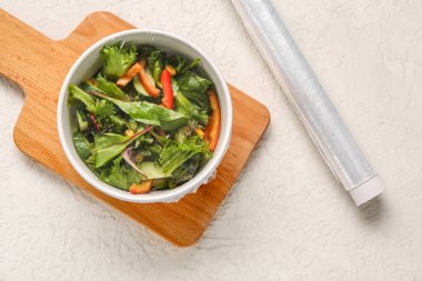 Hafif arka planda plastik gıda ambalajıyla kaplı bir kase taze salata.
