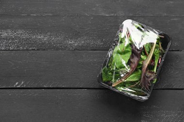 Siyah ahşap arka planda plastik gıda ambalajıyla kaplı taze salata yaprakları.