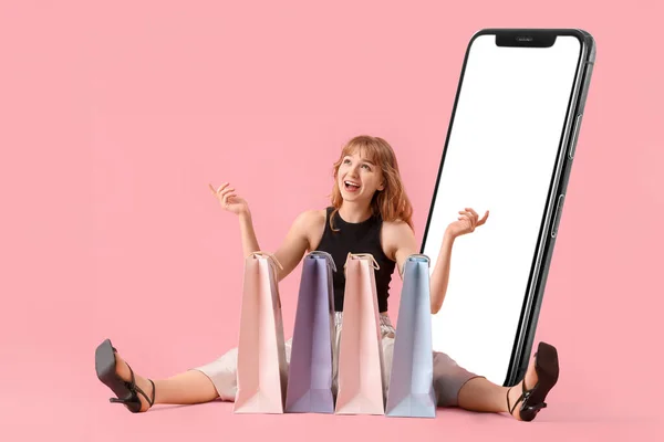Siedząca Młoda Kobieta Torbami Zakupy Dużym Telefonem Komórkowym Różowym Tle — Zdjęcie stockowe