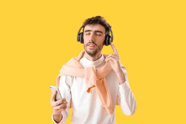 Sarı Arka Planda Cep Telefonu Olan Kulaklıklı Yakışıklı Bir Genç — Stok fotoğraf