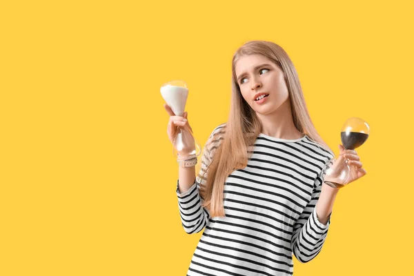 Stressed young woman with hourglass on yellow background. Deadline concept